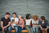 a group of people sitting on a bench with laptops